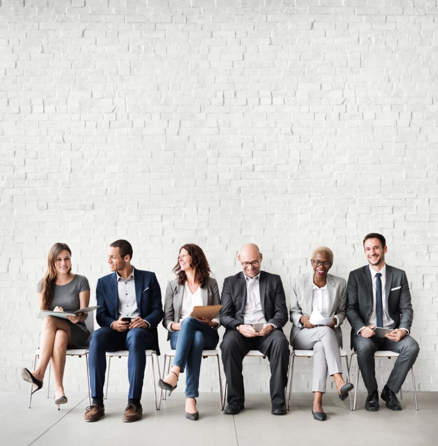 happy corporate colleagues sitting in chairs in front of a white wall.