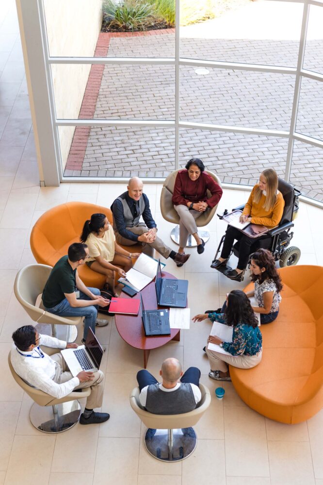 office colleagues working in colorful chairs in a huddle near large windows.