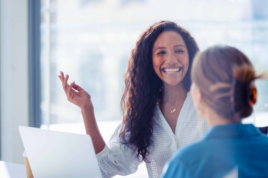 woman smiling and gesturing while talking to another woman.