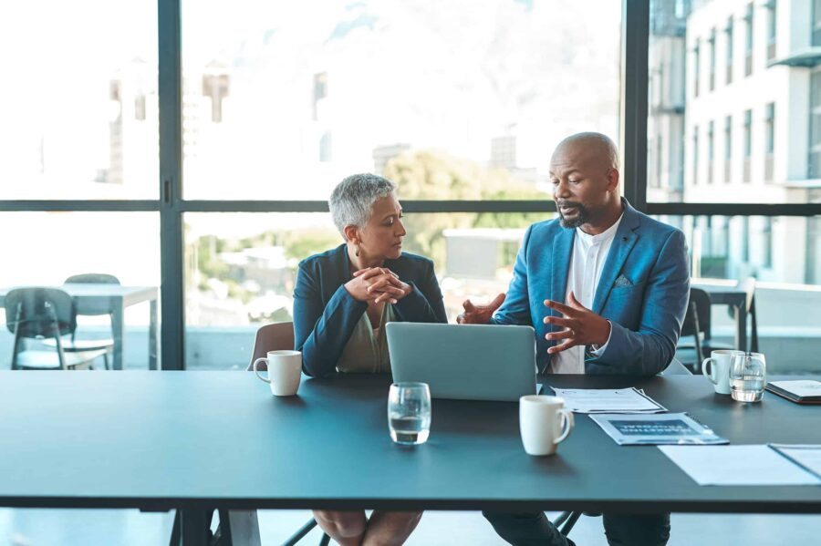 man and woman working together on a laptop in a corporate meeting room.